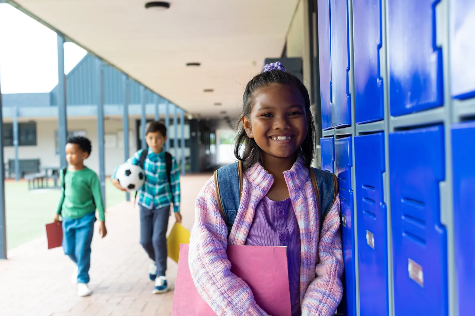 Smiling elementary student standing beside blue school lockers