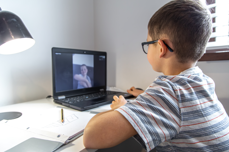 A young boy sitting at a desk with a laptop, focused on the screen.